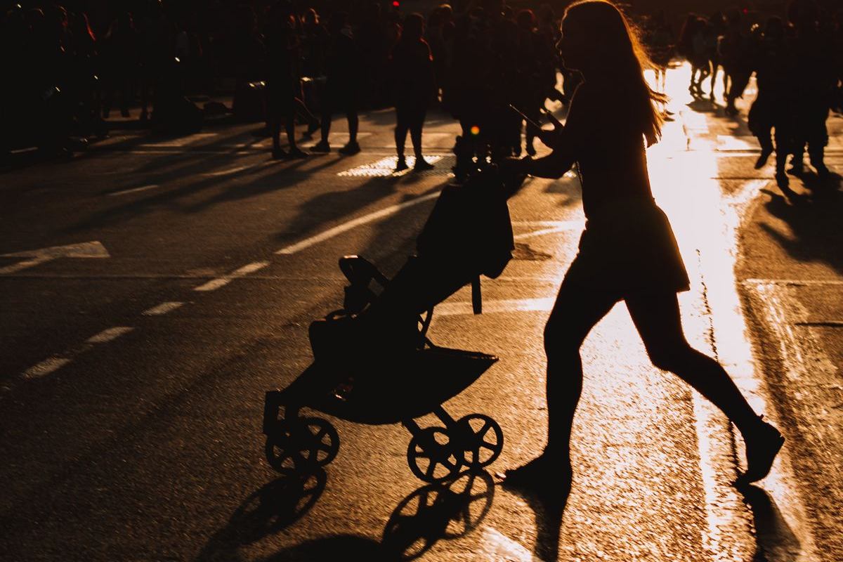 A parent pushing a stroller across a city street at sunset
